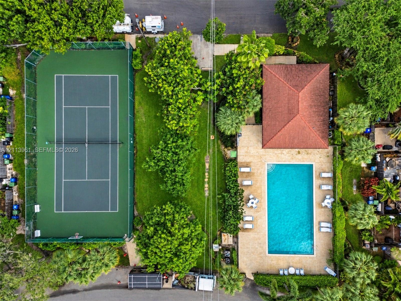 Fenced tennis court, rectangular swimming pool with stone-finish decking, and mature landscaping