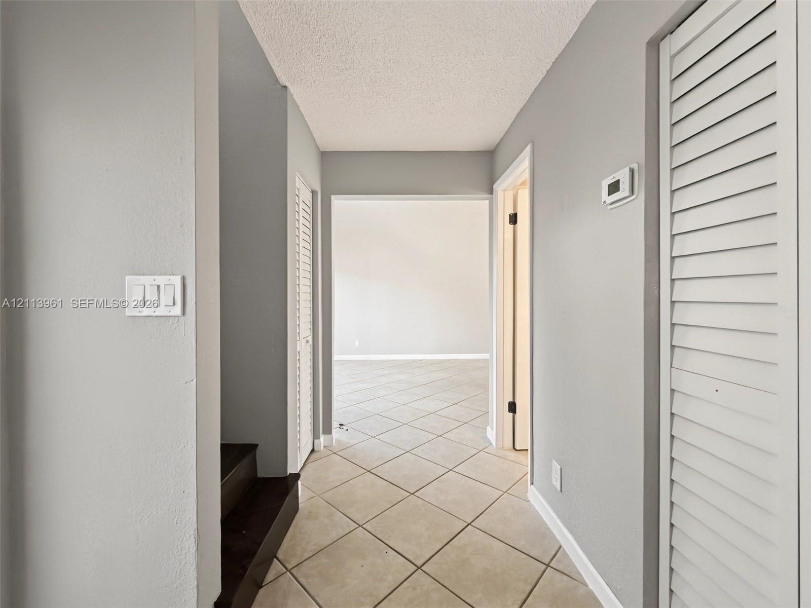 Interior hallway featuring tile flooring laid on a diagonal, dual louvered closet doors, and dark-finished staircase treads Interior hallway featuring tile flooring laid on a diagonal, dual louvered closet doors, and dark-finished staircase treads