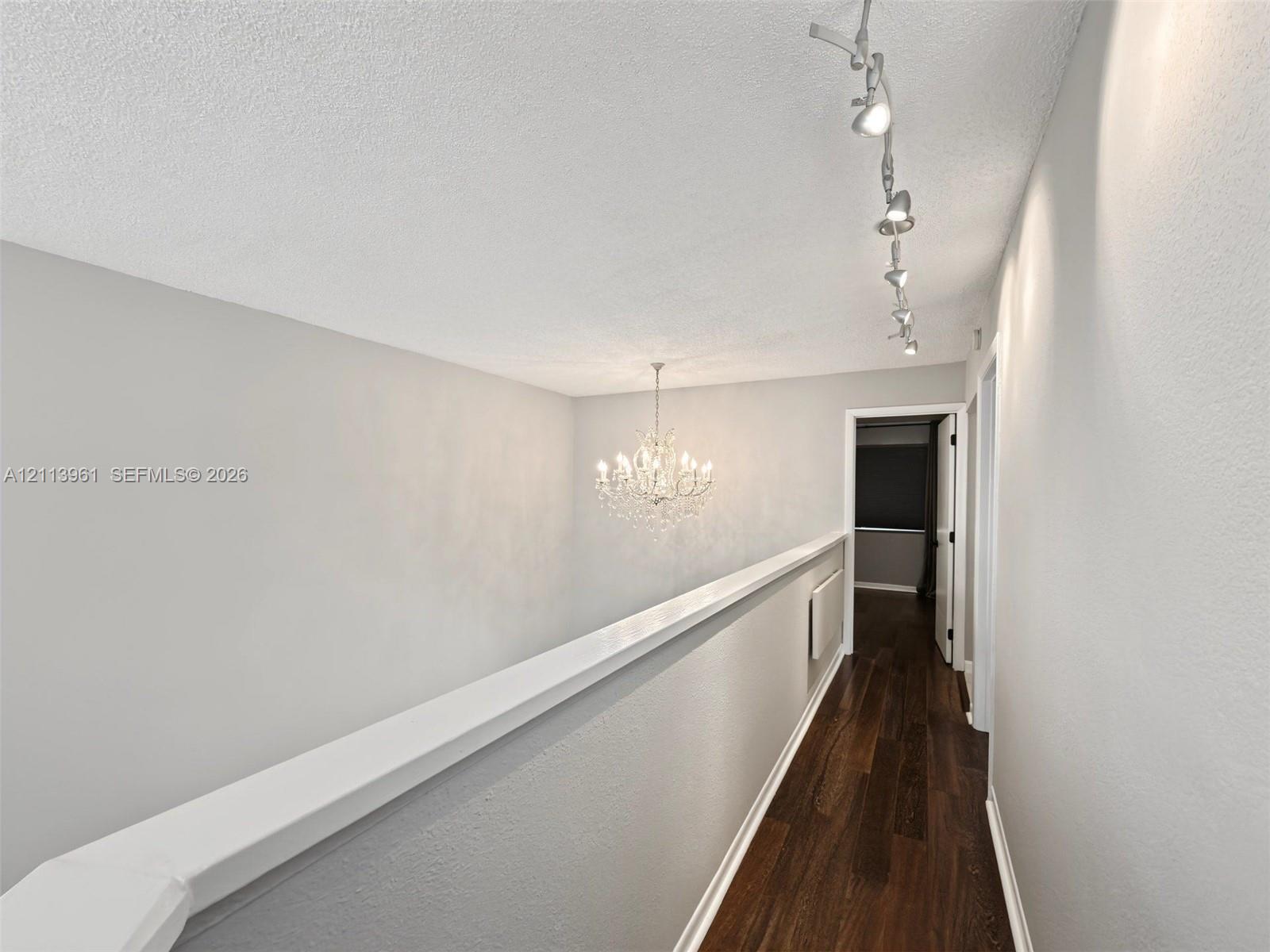 Hallway featuring dark wood-finish flooring, a multi-light crystal chandelier, and track lighting