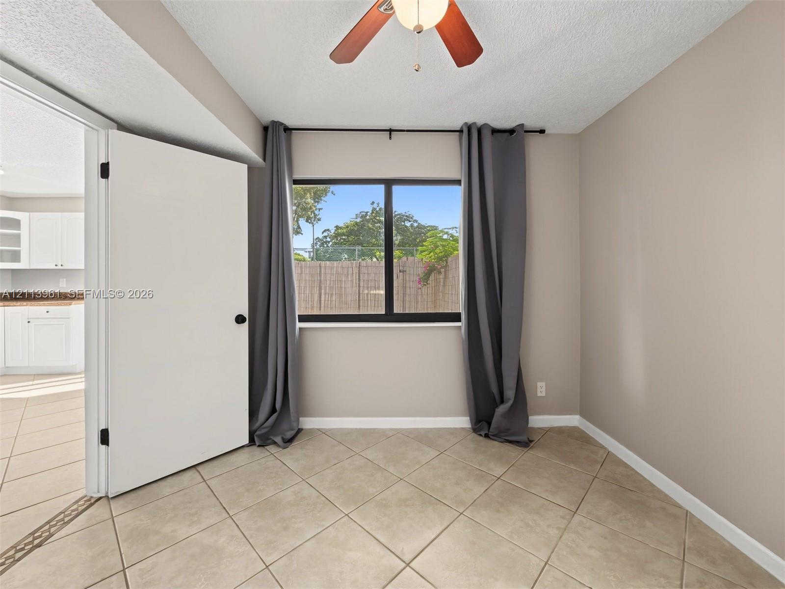 Interior space featuring neutral-toned walls, tile flooring, a window with a black frame, and an overhead ceiling fan with integrated lighting