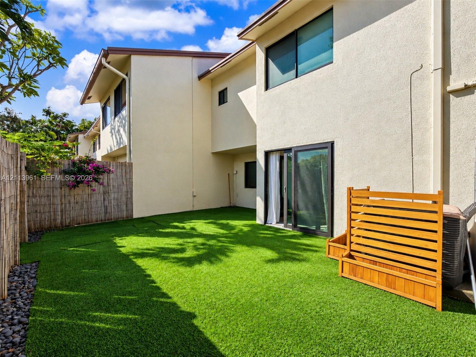Private outdoor space featuring artificial turf, perimeter bamboo fencing, river rock border, and a wood privacy screen