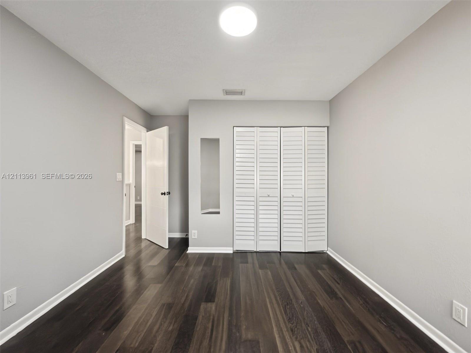 Room featuring wood-finish flooring, white louvered closet doors, and a neutral wall palette