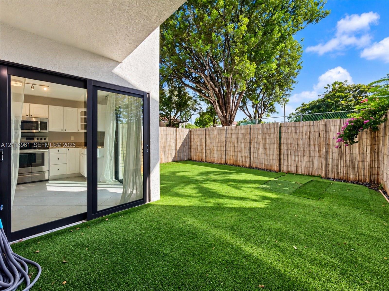 Private backyard featuring synthetic turf, perimeter fencing, and mature trees, complemented by a covered patio with sliding glass doors