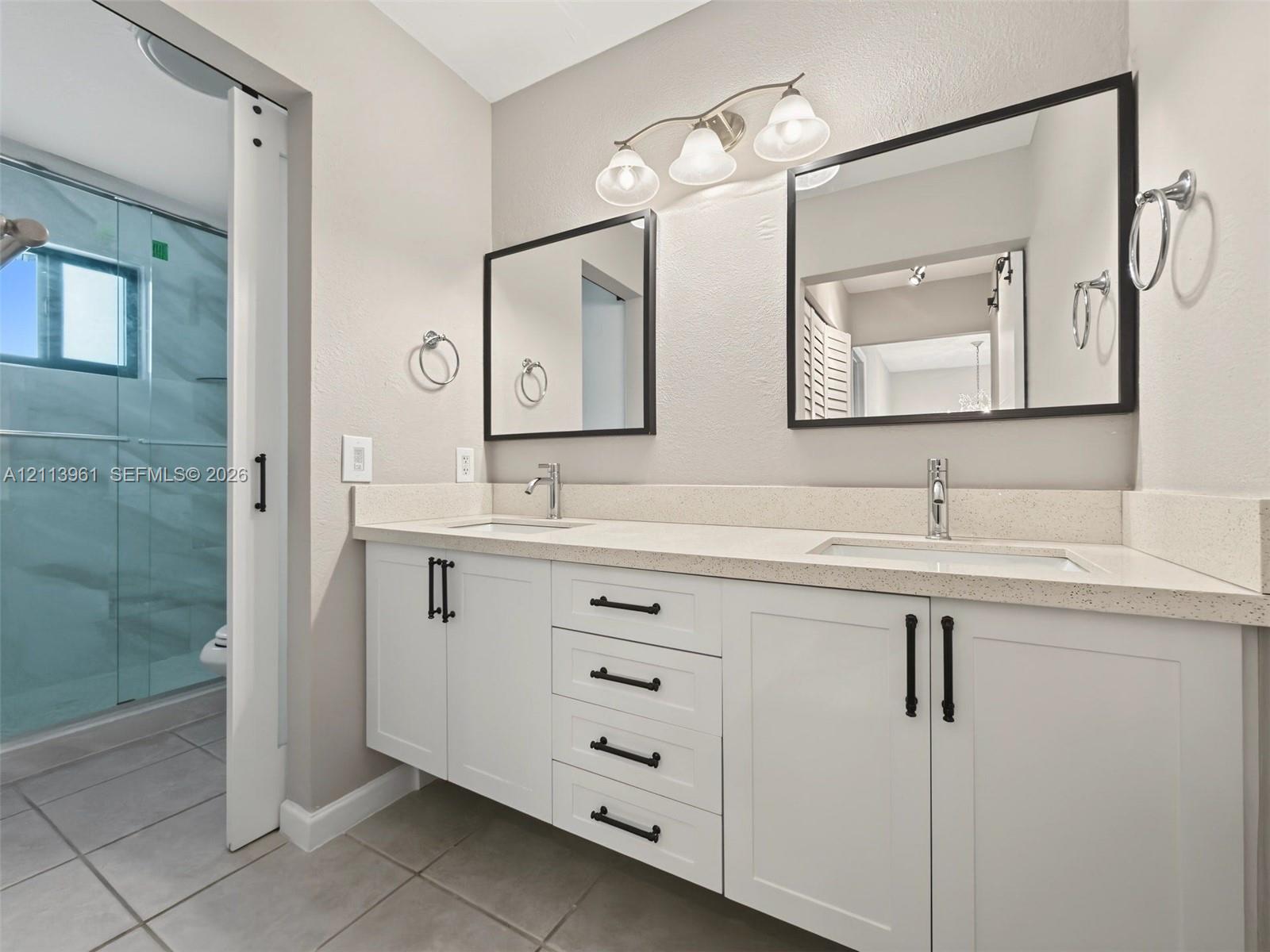 Dual-sink vanity with white shaker-style cabinetry, quartz countertops, matte black hardware, and two framed mirrors