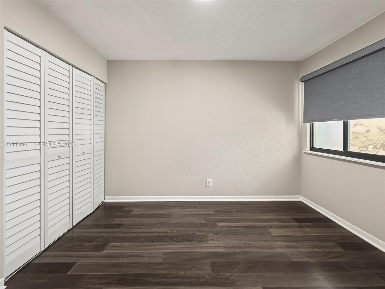 Neutral-toned walls, wood-finish flooring, and white louvered-style closet doors