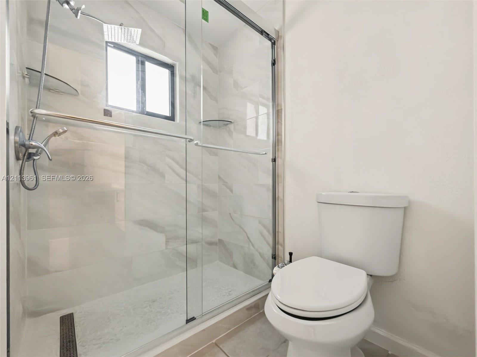 Walk-in shower featuring a frameless glass enclosure, polished stone-finish tile surround, integrated shelving, and a dual-function chrome shower head