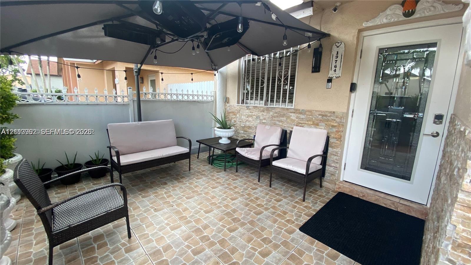 Covered patio featuring stone-tiled flooring, split-face stone veneer wall detailing, and a white entry door with an integrated glass panel