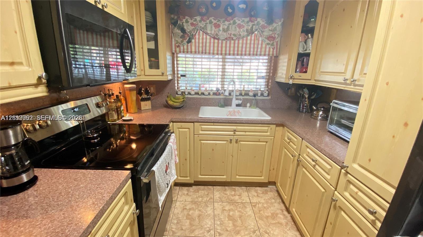 Kitchen featuring custom cabinetry, solid surface countertops, integrated double-basin sink, and ceramic tile flooring Kitchen featuring custom cabinetry, solid surface countertops, integrated double-basin sink, and ceramic tile flooring