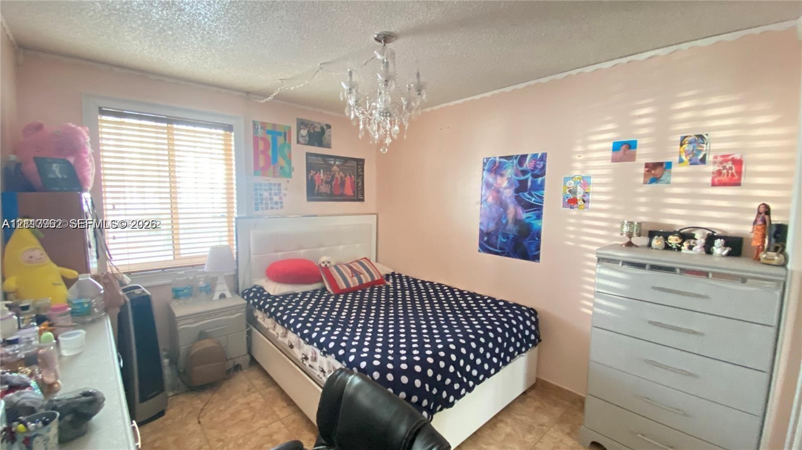 Room featuring horizontal blinds, tile flooring, and a central crystal-style chandelier fixture Room featuring horizontal blinds, tile flooring, and a central crystal-style chandelier fixture