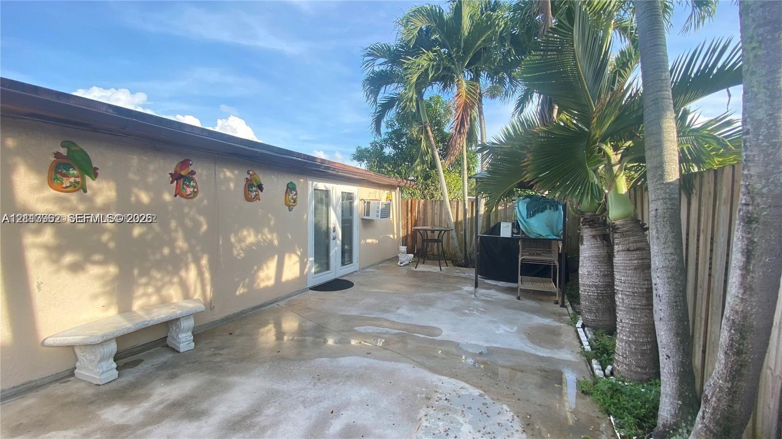 Concrete patio area enclosed by a wood privacy fence and featuring integrated palm trees