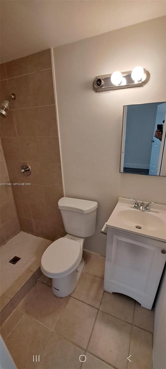 Bathroom featuring a tiled shower enclosure, white vanity cabinet with a integrated sink, two-light wall-mounted fixture, and ceramic floor tiling Bathroom featuring a tiled shower enclosure, white vanity cabinet with a integrated sink, two-light wall-mounted fixture, and ceramic floor tiling