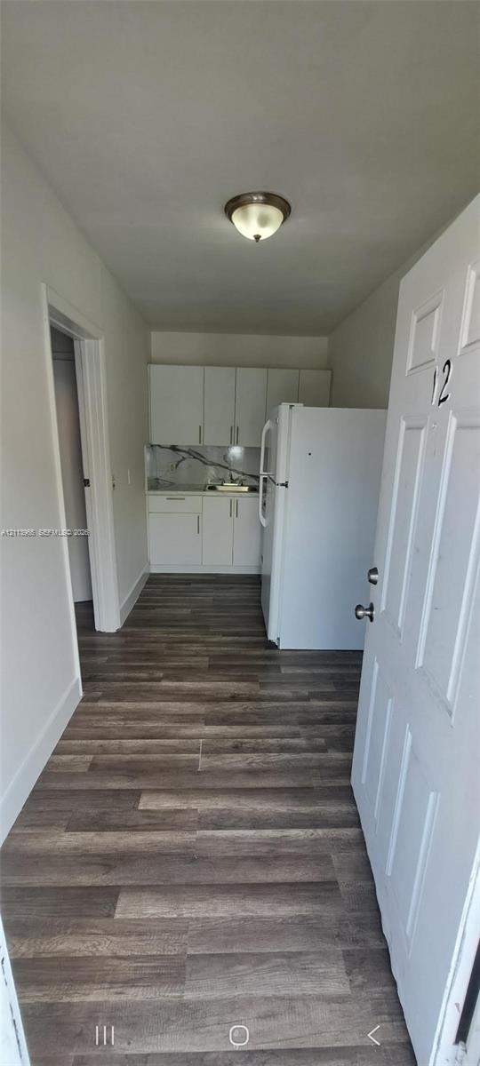 Kitchen area featuring white cabinetry, wood-finish flooring, and a stone-patterned backsplash Kitchen area featuring white cabinetry, wood-finish flooring, and a stone-patterned backsplash