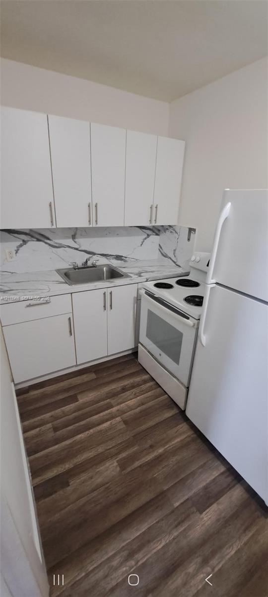 Kitchen featuring white shaker-style cabinetry, high-contrast patterned backsplash, stainless steel sink, electric range, and wood-finish flooring Kitchen featuring white shaker-style cabinetry, high-contrast patterned backsplash, stainless steel sink, electric range, and wood-finish flooring