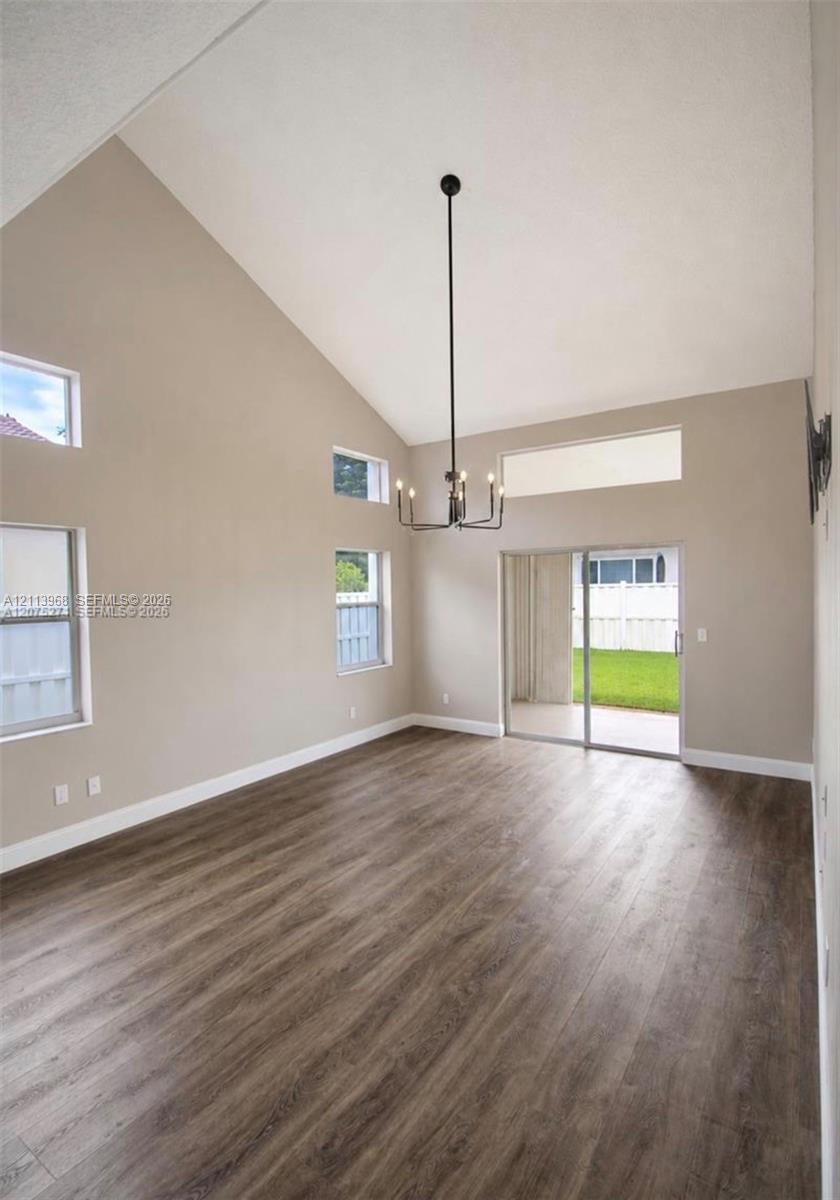 Vaulted ceilings, wood-finish flooring, multi-level windows, modern chandelier, and sliding glass doors