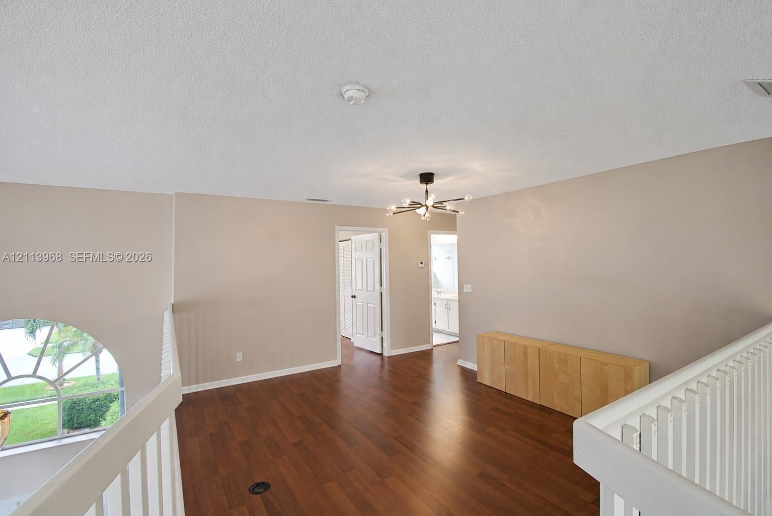 Open loft area featuring wood-finish flooring, a contemporary multi-arm chandelier, an arched window with decorative muntins, and white-painted millwork railings