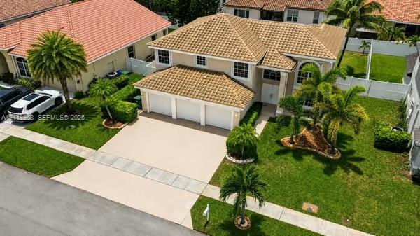 Two-story residence featuring a tile roof, three-car garage, concrete driveway, and landscaped yard with palm trees