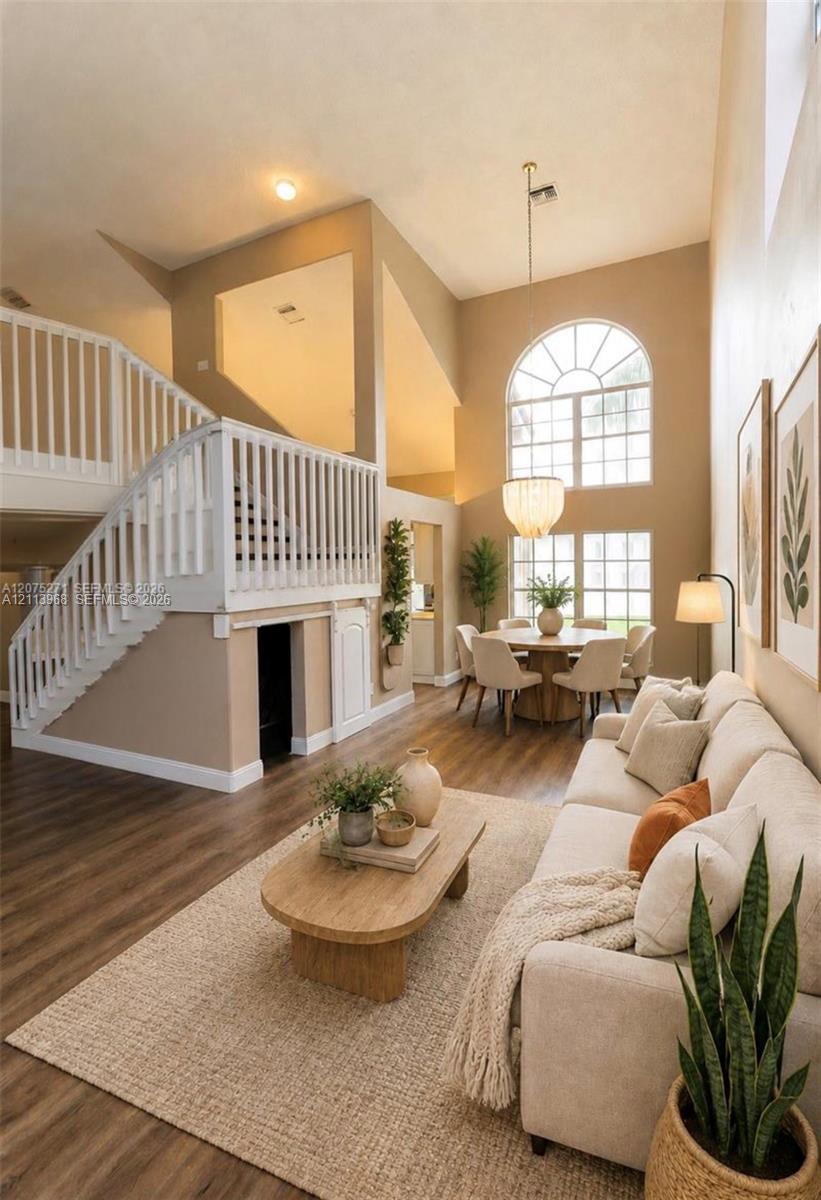 Vaulted ceilings featuring double-height windows with arched transom, wood-finish flooring, and a staircase with white vertical balusters and a built-in lower storage cabinet