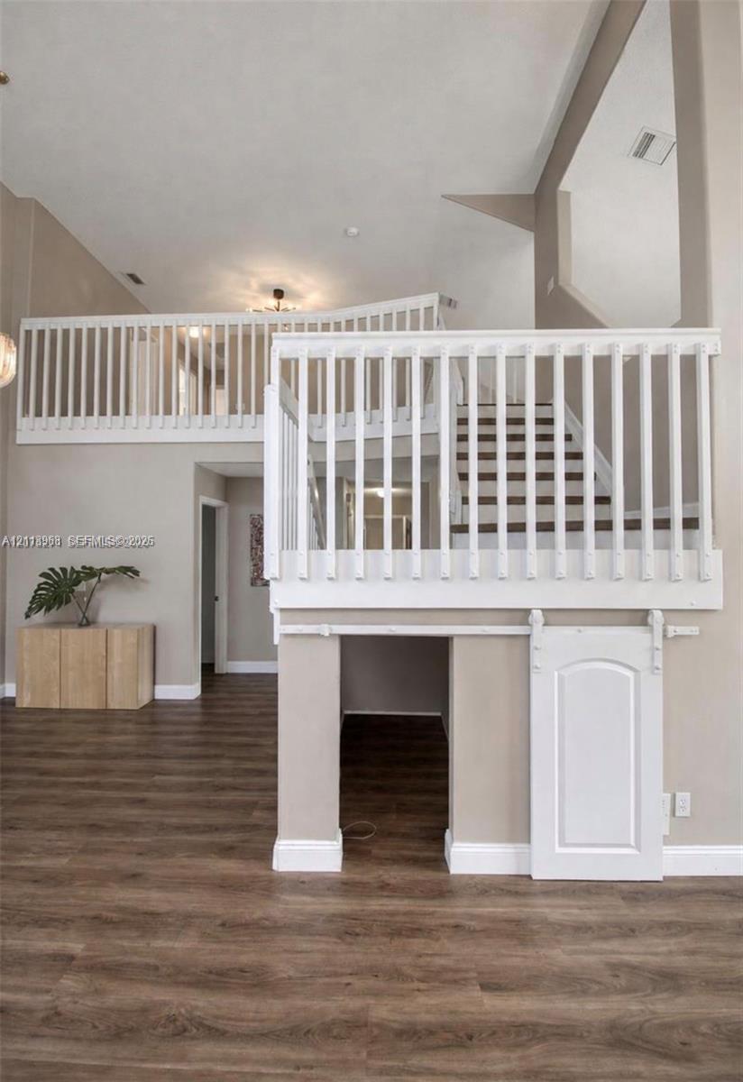 High-ceiling interior featuring wood-finish flooring, a white wooden staircase balustrade, and a lower-level built-in storage area with a sliding barn-style door High-ceiling interior featuring wood-finish flooring, a white wooden staircase balustrade, and a lower-level built-in storage area with a sliding barn-style door