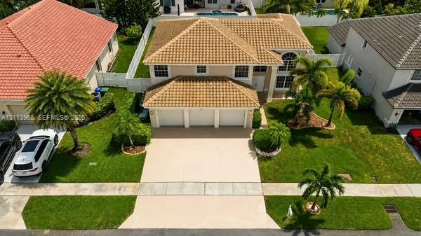 Two-story residence featuring a tile roof, three-car garage, concrete driveway, and landscaped lawn with mature palm trees Two-story residence featuring a tile roof, three-car garage, concrete driveway, and landscaped lawn with mature palm trees