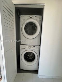 Stacked laundry center featuring a white front-load washing machine, white front-load dryer, and louvered closet door
