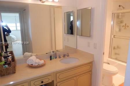 Bathroom featuring a vanity with a solid-surface countertop, recessed oval sink, full-width wall mirror, and a tub-shower combination with sliding glass doors Bathroom featuring a vanity with a solid-surface countertop, recessed oval sink, full-width wall mirror, and a tub-shower combination with sliding glass doors