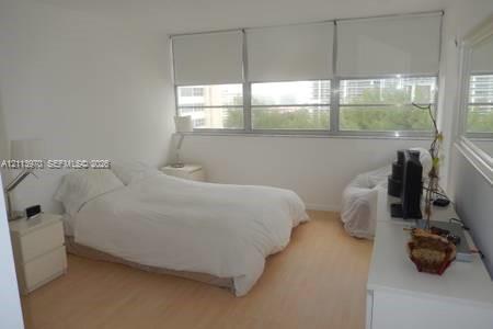 Room featuring wood-finish flooring, a wall-to-wall window configuration, roller shades, and a large wall-mounted mirror Room featuring wood-finish flooring, a wall-to-wall window configuration, roller shades, and a large wall-mounted mirror