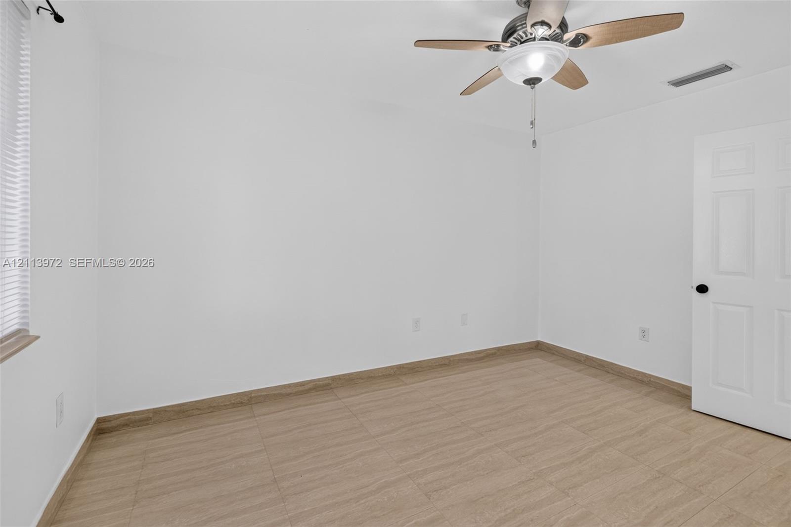 Neutral interior featuring wood-finish tile flooring, a multi-blade ceiling fan with integrated lighting, and a six-panel interior door
