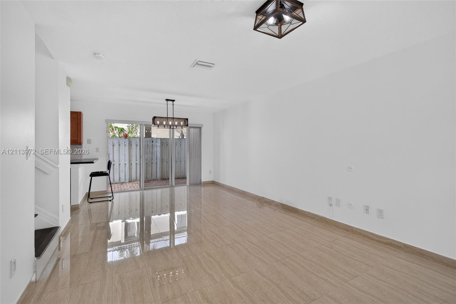Open-concept interior featuring large-format tile flooring, modern geometric ceiling lighting, and sliding glass doors providing outdoor access Open-concept interior featuring large-format tile flooring, modern geometric ceiling lighting, and sliding glass doors providing outdoor access