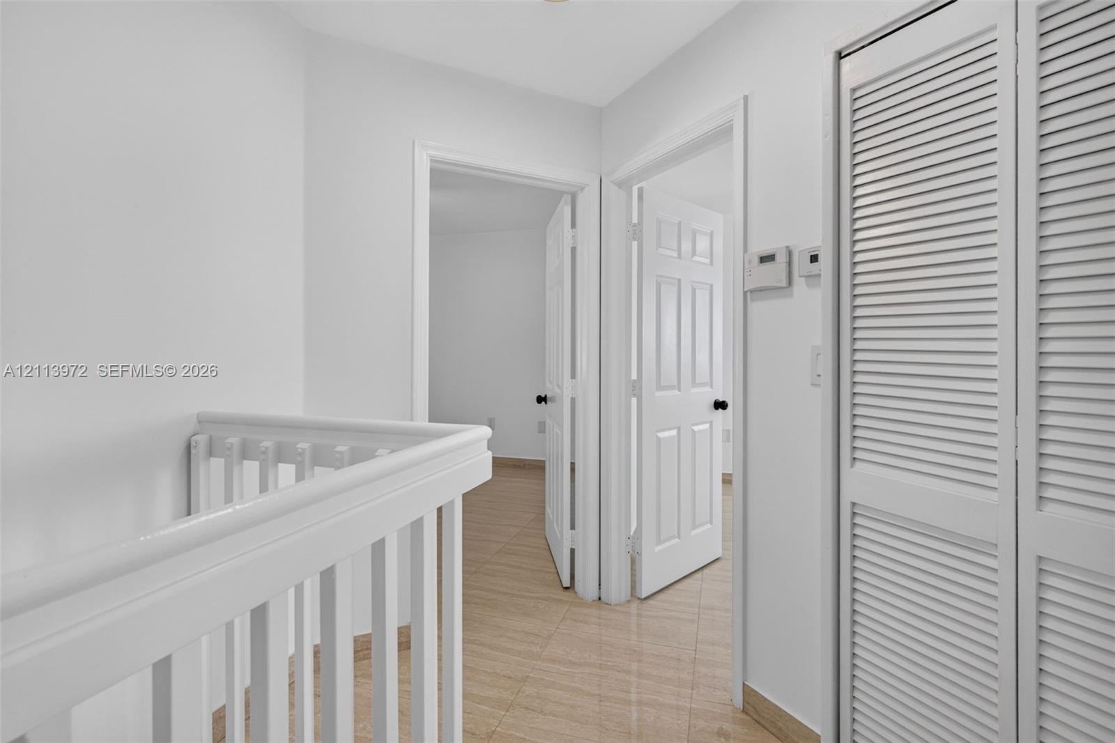 White wood-finish railings, neutral tile flooring, six-panel interior doors, and floor-to-ceiling louvered closet doors