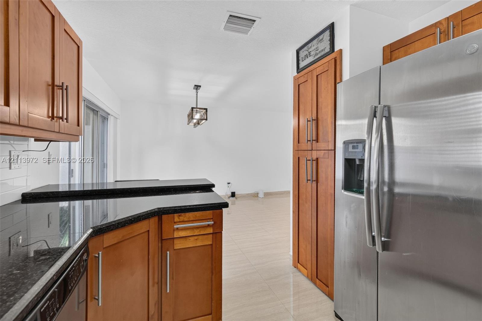 Kitchen featuring wood cabinetry, stone countertops, stainless steel side-by-side refrigerator, tile flooring, and metal pendant lighting
