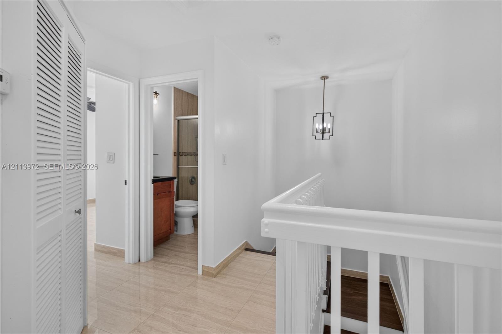 Louvered bi-fold closet doors, tile flooring, white-painted wooden railings, and a hanging geometric pendant light fixture