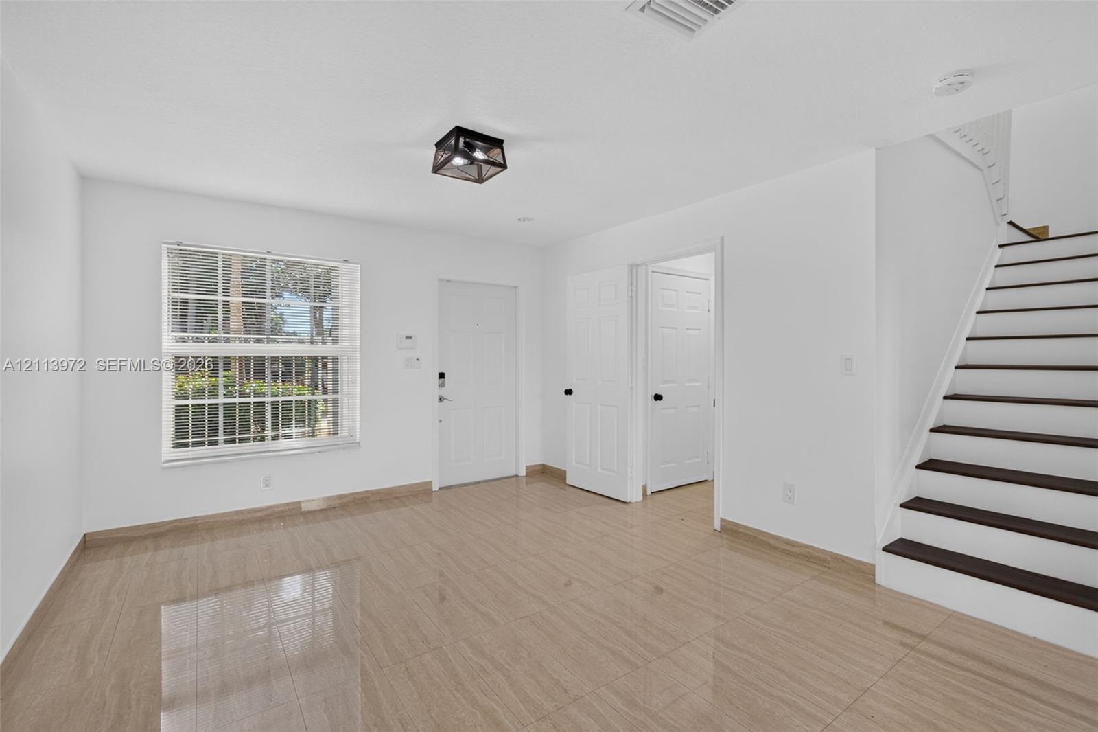 Neutral-tone tile flooring, multi-pane window, flush-mount geometric ceiling light, and staircase with dark wood-finish treads Neutral-tone tile flooring, multi-pane window, flush-mount geometric ceiling light, and staircase with dark wood-finish treads