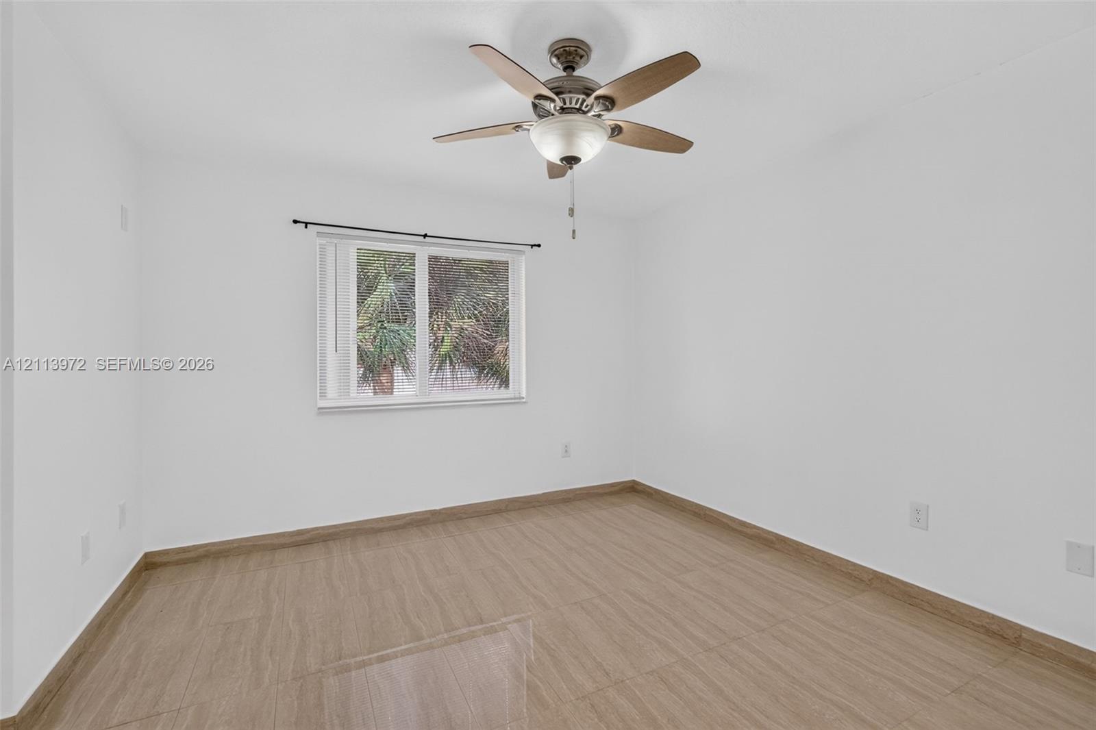 Interior room featuring wood-finish flooring, a multi-blade ceiling fan with integrated lighting, and a window with a curtain rod