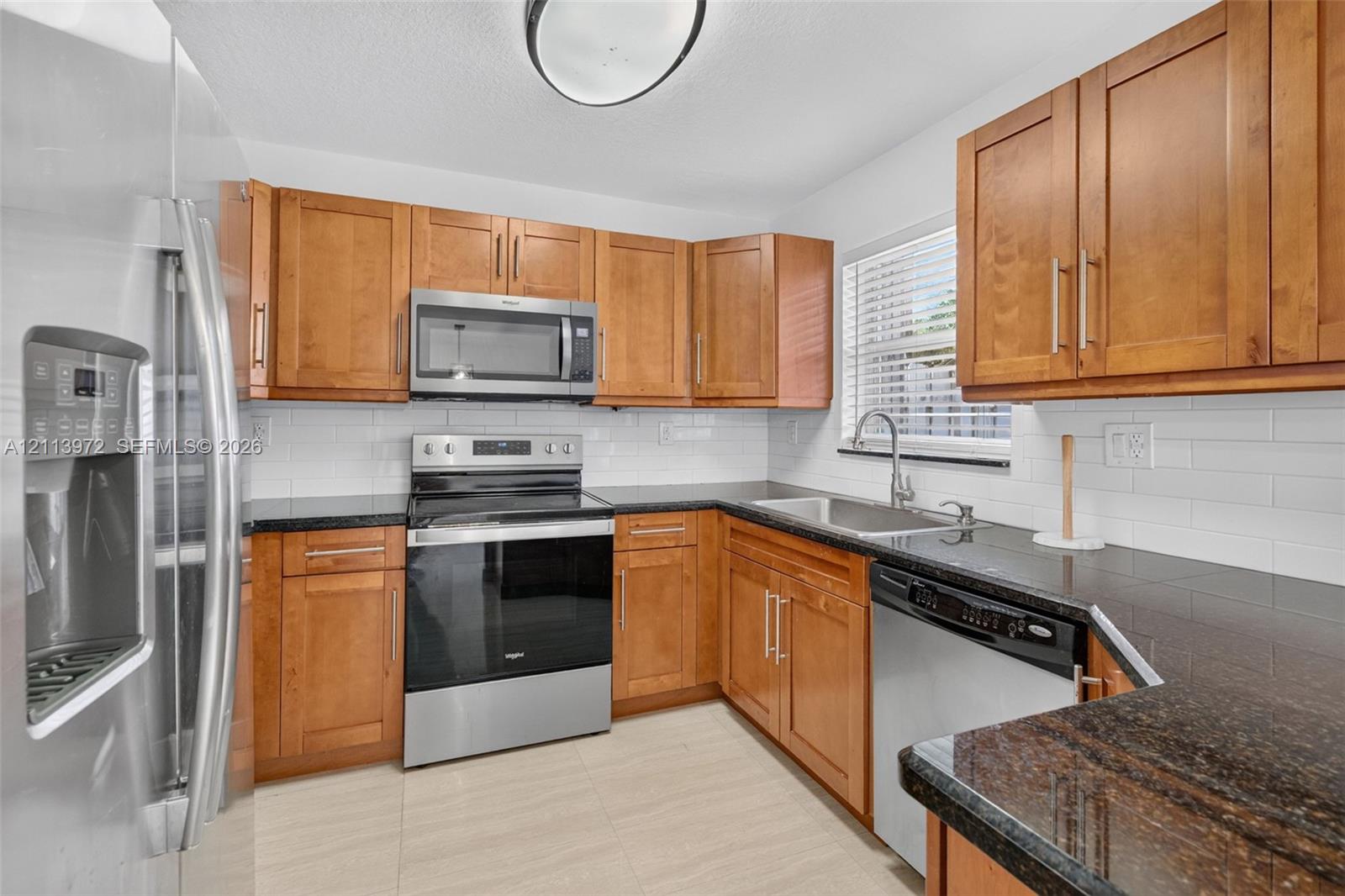 Kitchen featuring wood cabinetry, stone countertops, a subway tile backsplash, and stainless steel appliances