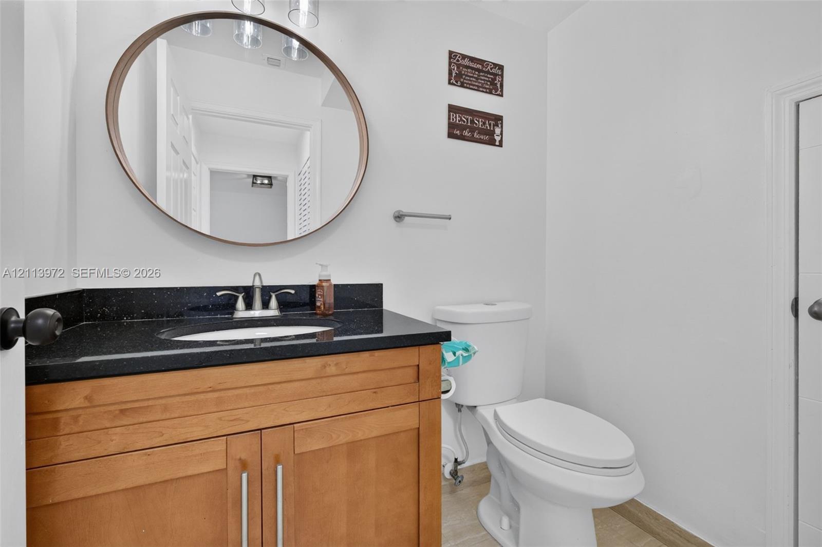 Wood-finish vanity cabinet, dark stone-surfaced countertop, integrated oval sink, chrome dual-handle faucet, and oval-framed wall mirror