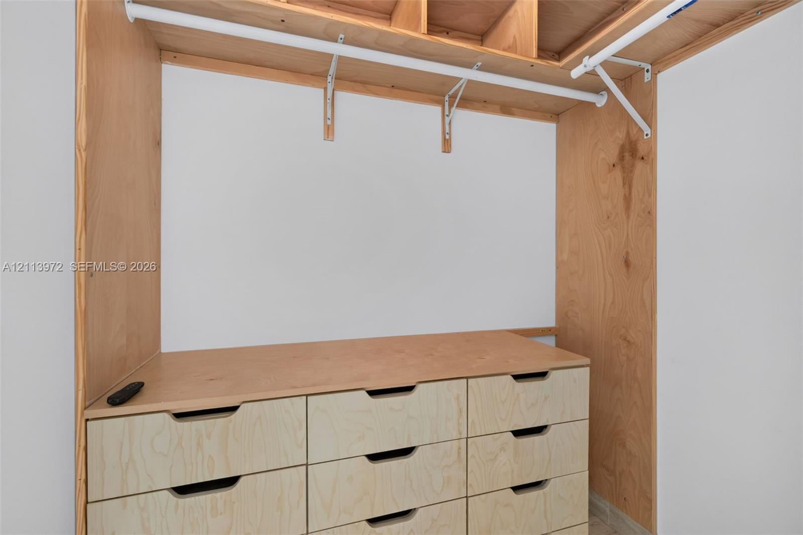 Custom-built storage featuring light wood cabinetry, integrated drawer units, open shelving, and white metal garment rods
