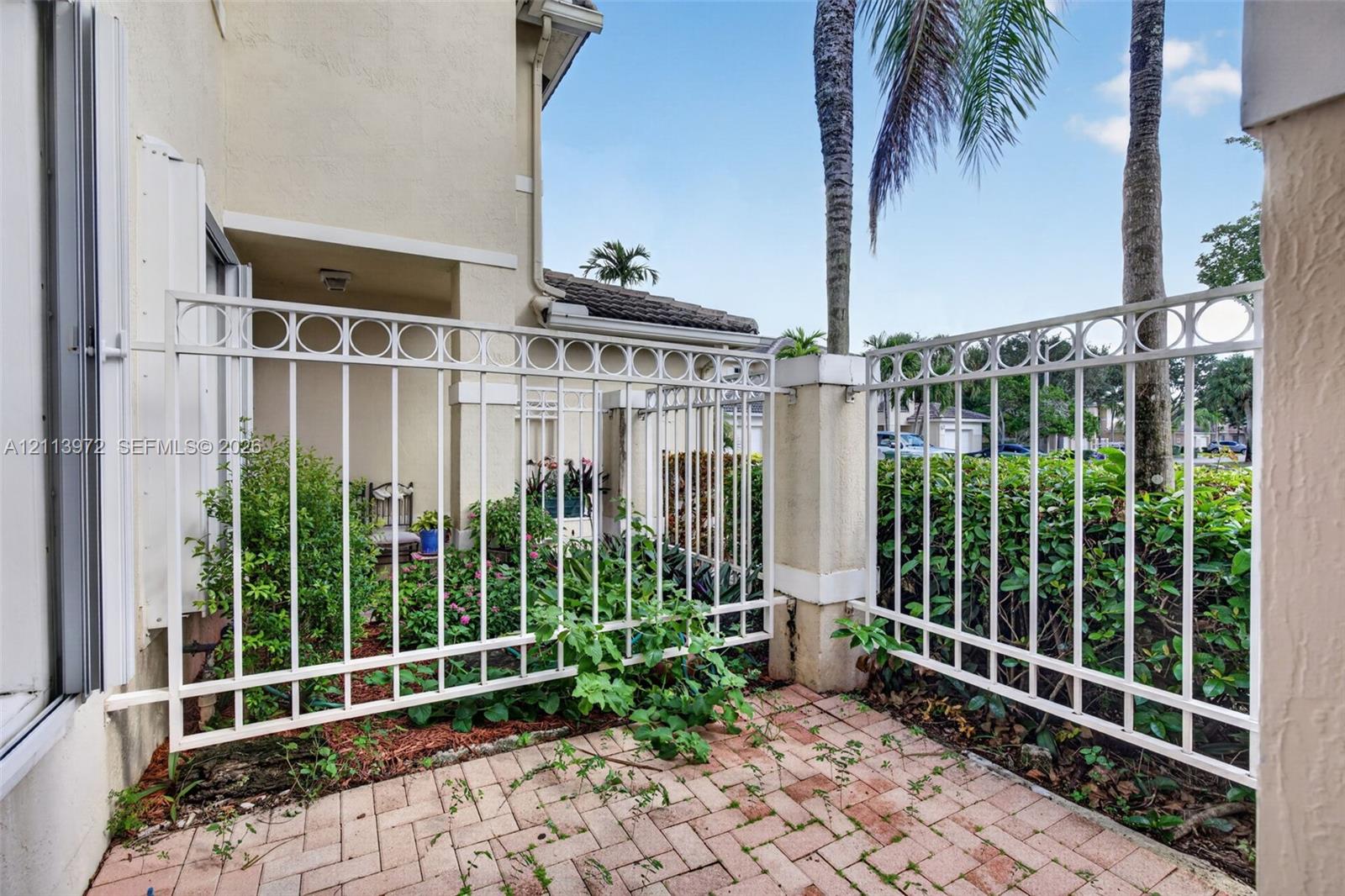 Private patio featuring herringbone-patterned brick pavers, a decorative white metal fence, and stucco exterior walls