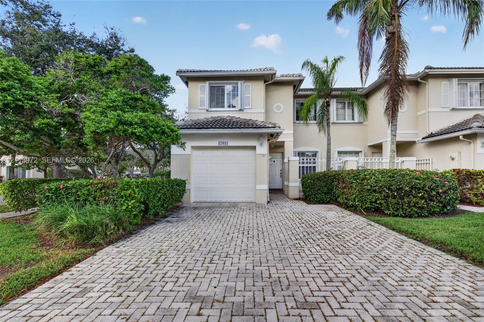 Two-story exterior featuring a stucco facade, tiled roof, attached single-car garage, and paved herringbone-pattern driveway Two-story exterior featuring a stucco facade, tiled roof, attached single-car garage, and paved herringbone-pattern driveway