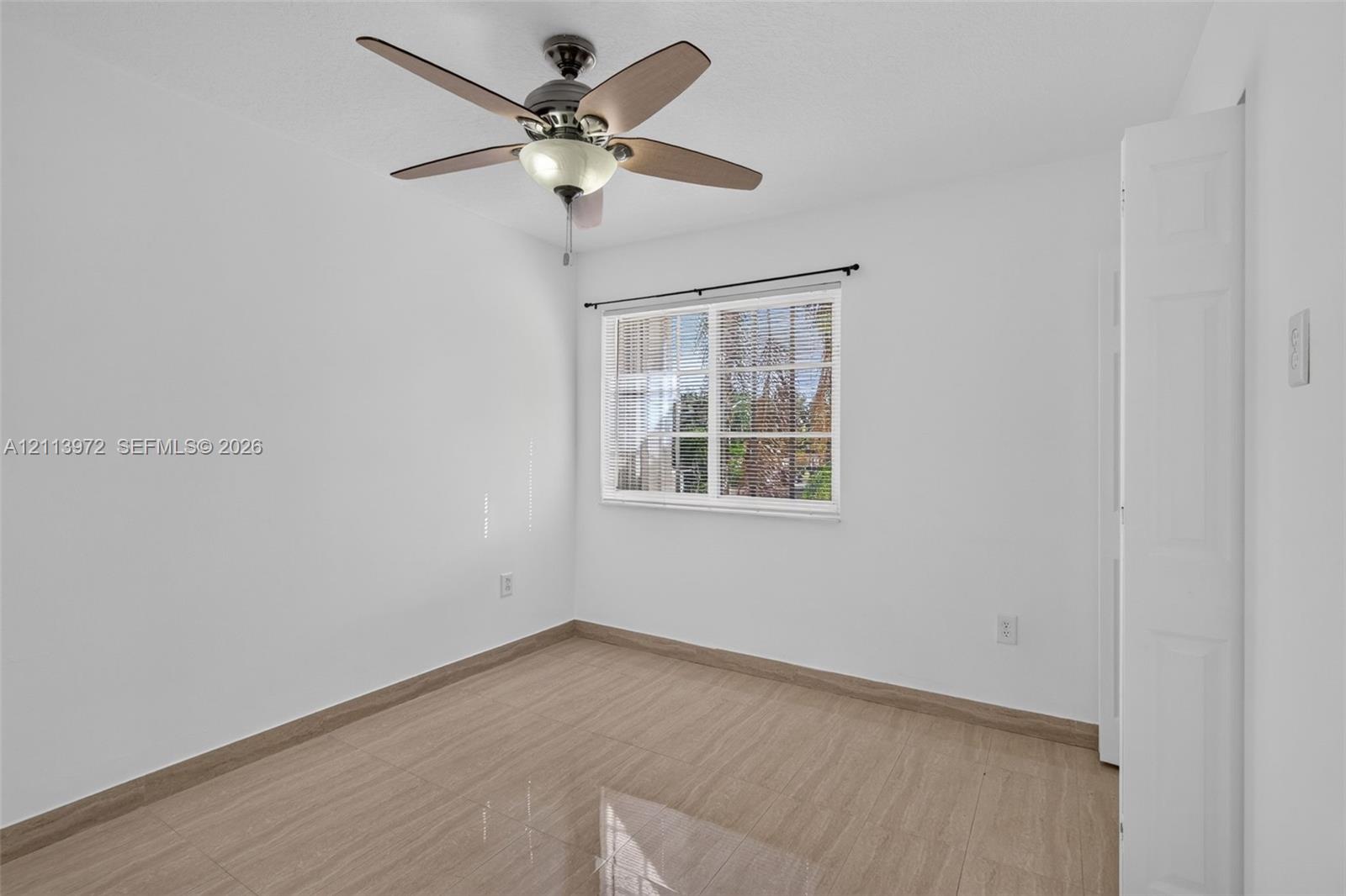 Room featuring wood-finish tile flooring, ceiling fan with integrated lighting, window with horizontal blinds, and a multi-panel door