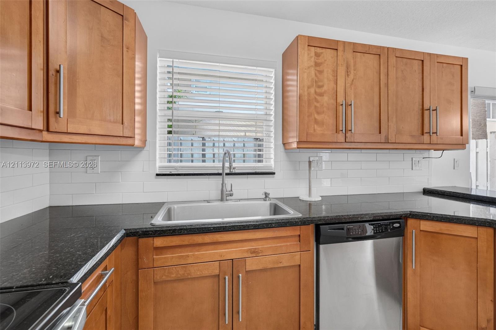 Kitchen featuring shaker-style cabinetry, dark stone countertops, white subway tile backsplash, stainless steel dishwasher, and undermount sink with gooseneck faucet