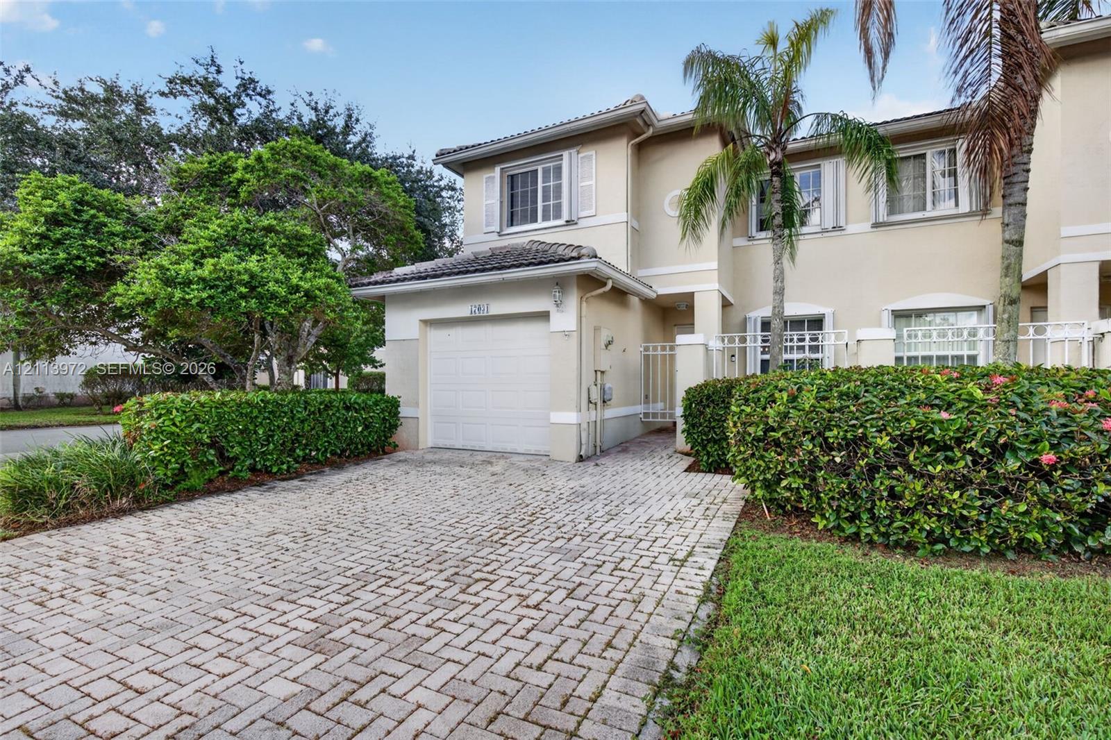 Two-story stucco exterior featuring a paver driveway, single-car garage, manicured landscaping, and decorative shutters Two-story stucco exterior featuring a paver driveway, single-car garage, manicured landscaping, and decorative shutters
