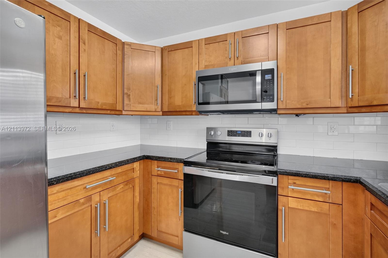 Kitchen featuring wood cabinetry, stainless steel appliances, dark stone-finish countertops, and a white subway tile backsplash