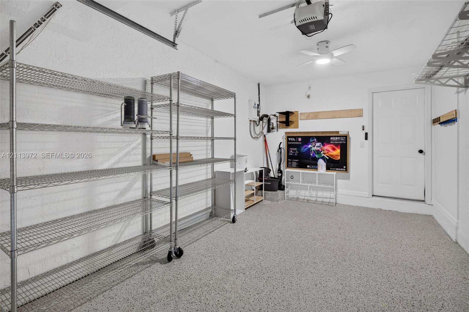Garage space featuring epoxy flooring, textured walls, ceiling-mounted light fixture, and overhead storage shelving