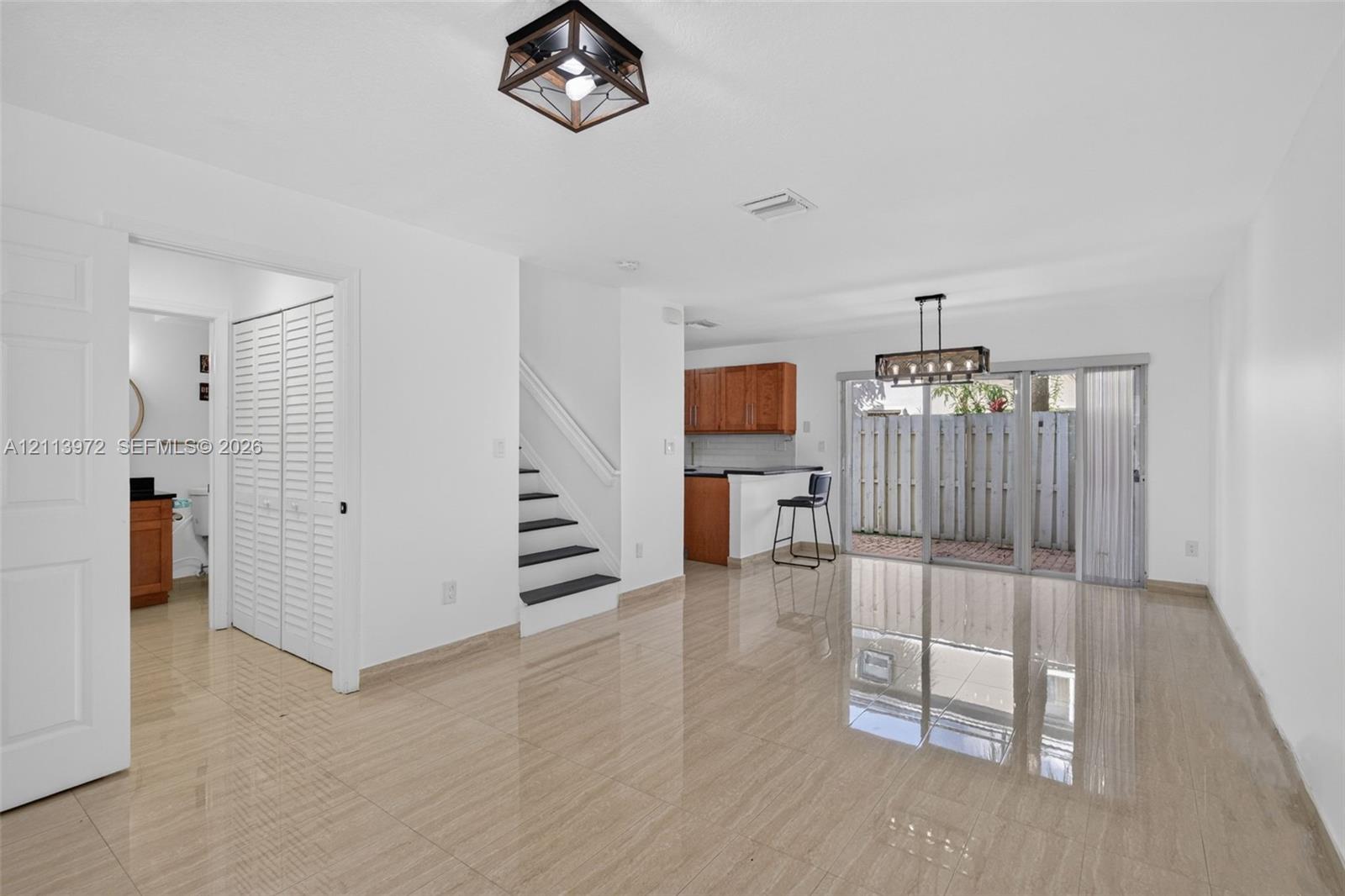 Open-concept interior featuring large-format tile flooring, a lantern-style flush mount ceiling light, an iron and glass chandelier, a staircase with contrast treads, and sliding glass doors Open-concept interior featuring large-format tile flooring, a lantern-style flush mount ceiling light, an iron and glass chandelier, a staircase with contrast treads, and sliding glass doors
