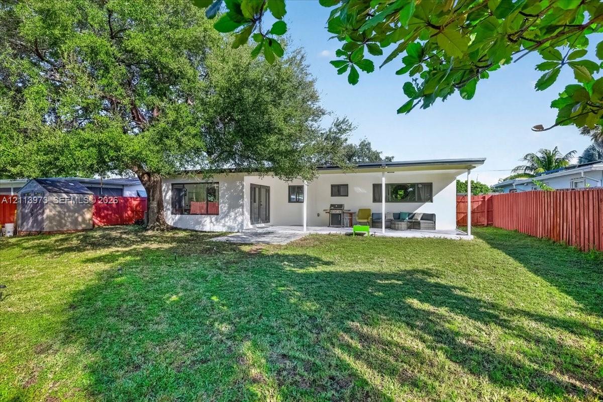 Expansive backyard featuring a large shade tree, covered patio, wood-style privacy fencing, and exterior storage structure