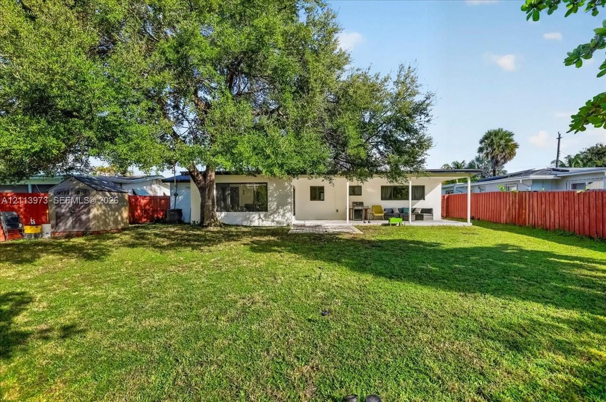 Backyard featuring a covered patio, expansive lawn, mature canopy trees, and privacy fencing