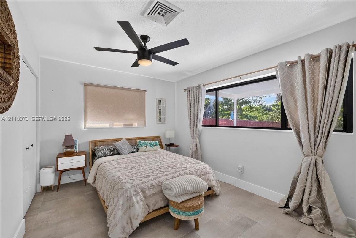 Bedroom featuring large-format tile flooring, matte black ceiling fan with integrated lighting, oversized horizontal window with black trim, and white closet doors with dark hardware