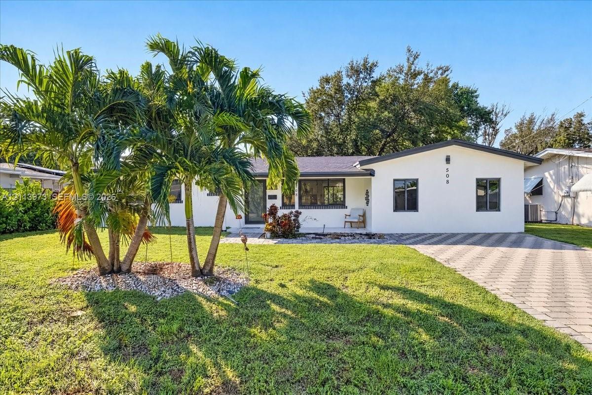 Single-story exterior featuring white stucco siding, a paved stone driveway, dark-trimmed window frames, and established palm tree landscaping Single-story exterior featuring white stucco siding, a paved stone driveway, dark-trimmed window frames, and established palm tree landscaping
