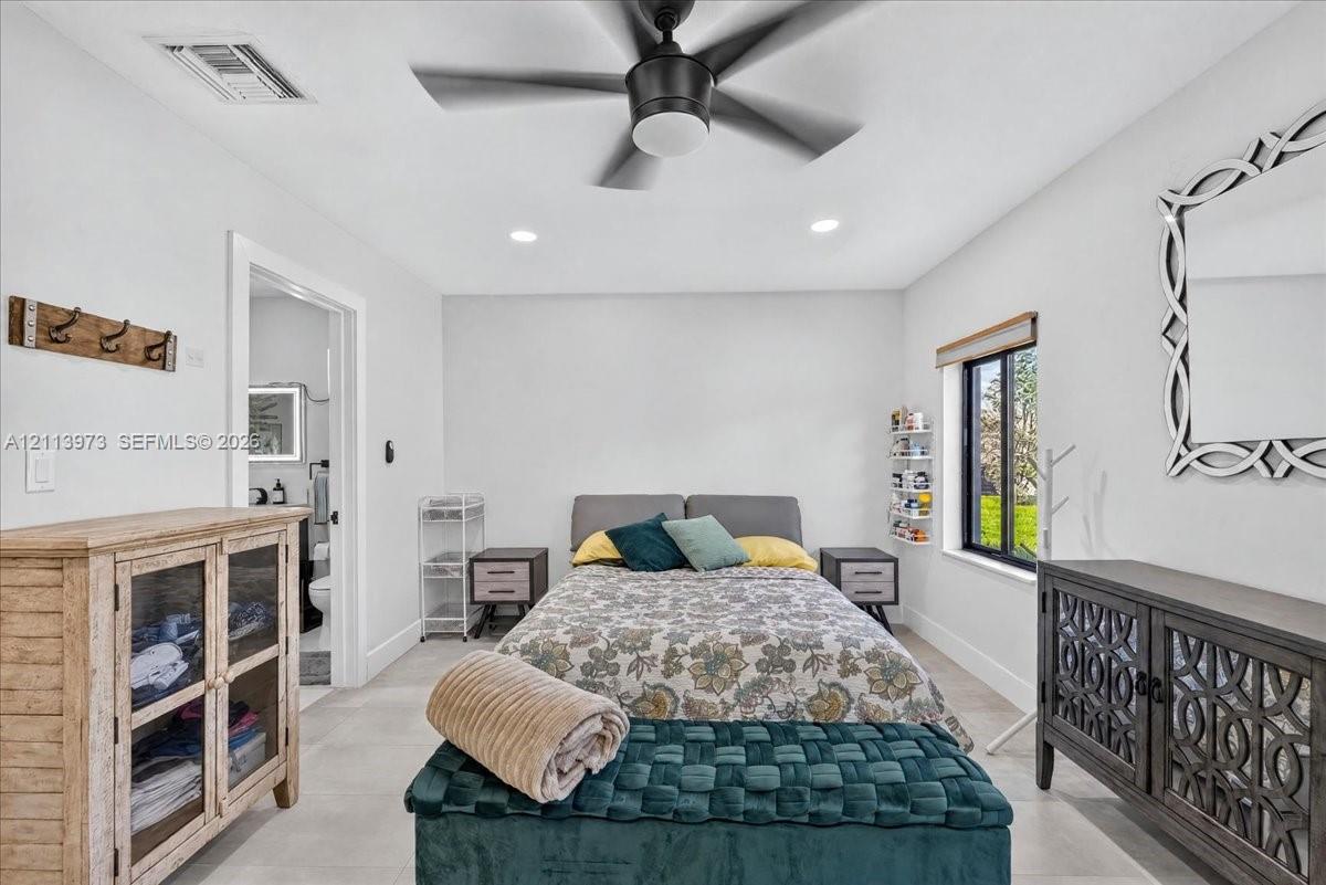 Neutral-toned interior space featuring tile flooring, a central ceiling fan with an integrated light fixture, recessed lighting, and a window with a roller shade