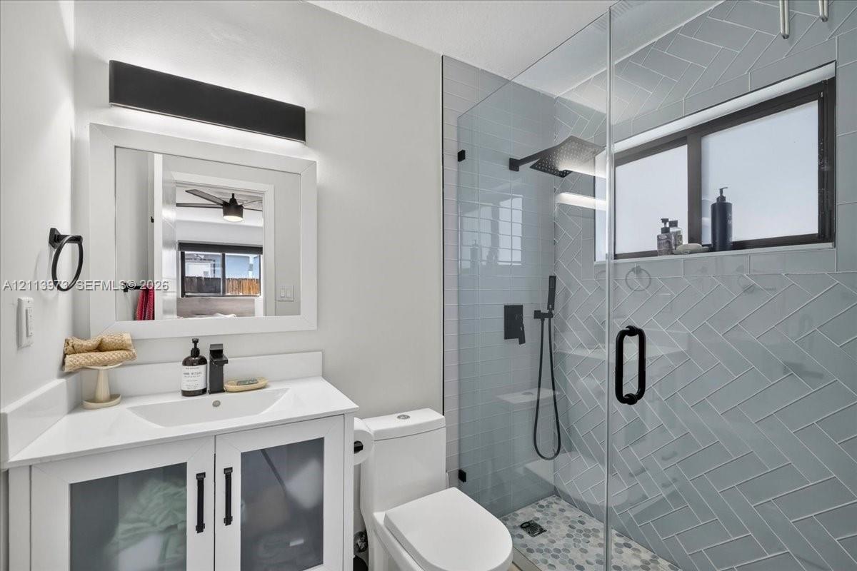 White vanity with a rectangular sink, herringbone-patterned wall tile, glass-enclosed shower with matte black fixtures, and custom light fixture